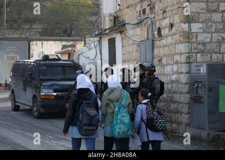 28. November 2021: Nablus, Palästina. 28. November 2021. Palästinensische Schulkinder gehen auf dem Weg zur Schule unter den wachsamen Augen israelischer Soldaten im Dorf Lubban Ash-Sharqiya, südlich von Nablus. Das Dorf und die Schulen wurden kürzlich täglich von jüdisch-israelischen Siedlern angegriffen, die ebenfalls versucht haben, den Zugang der Schüler zur Schule zu behindern. Die Bewohner organisieren Proteste gegen die Gewalt der Siedler, wobei israelische Kräfte die Demonstrationen unterdrücken und einige ihrer Teilnehmer verhaften (Foto: © Mohammed Turabi/IMAGESLIVE via ZUMA Press Wire) Stockfoto