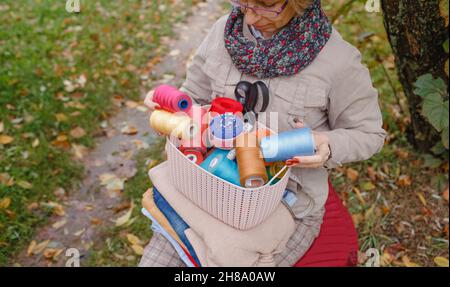 Eine Näherin sitzt auf der Straße und hält einen Korb mit bunten Nähfäden und Nadeln. Stockfoto