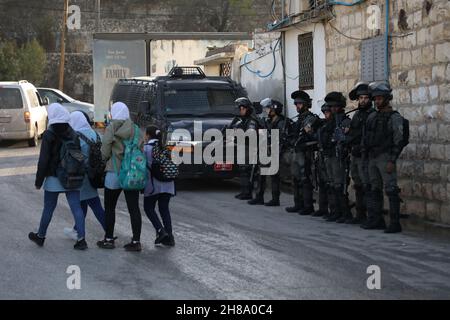 28. November 2021: Nablus, Palästina. 28. November 2021. Palästinensische Schulkinder gehen auf dem Weg zur Schule unter den wachsamen Augen israelischer Soldaten im Dorf Lubban Ash-Sharqiya, südlich von Nablus. Das Dorf und die Schulen wurden kürzlich täglich von jüdisch-israelischen Siedlern angegriffen, die ebenfalls versucht haben, den Zugang der Schüler zur Schule zu behindern. Die Bewohner organisieren Proteste gegen die Gewalt der Siedler, wobei israelische Kräfte die Demonstrationen unterdrücken und einige ihrer Teilnehmer verhaften (Foto: © Mohammed Turabi/IMAGESLIVE via ZUMA Press Wire) Stockfoto