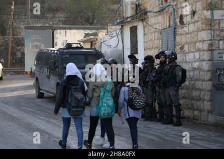 28. November 2021: Nablus, Palästina. 28. November 2021. Palästinensische Schulkinder gehen auf dem Weg zur Schule unter den wachsamen Augen israelischer Soldaten im Dorf Lubban Ash-Sharqiya, südlich von Nablus. Das Dorf und die Schulen wurden kürzlich täglich von jüdisch-israelischen Siedlern angegriffen, die ebenfalls versucht haben, den Zugang der Schüler zur Schule zu behindern. Die Bewohner organisieren Proteste gegen die Gewalt der Siedler, wobei israelische Kräfte die Demonstrationen unterdrücken und einige ihrer Teilnehmer verhaften (Foto: © Mohammed Turabi/IMAGESLIVE via ZUMA Press Wire) Stockfoto