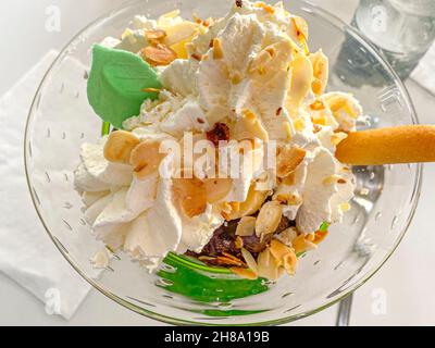 Eiskugeln mit Schlagsahne, Mandelkrume, Blattdeko in einer Glastasse auf dem Restauranttisch. Fotos in hoher Qualität Stockfoto