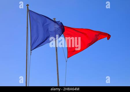 Zwei dreieckige Flaggen, die nebeneinander auf Masten angebracht sind, blasen zu Warn- und Informationszwecken im Wind. Stockfoto