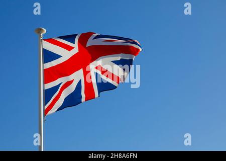 Die Nationalflagge des Vereinigten Königreichs flattert im Wind und kann an einem sonnigen Tag gegen einen blauen Himmel gesehen werden. Stockfoto