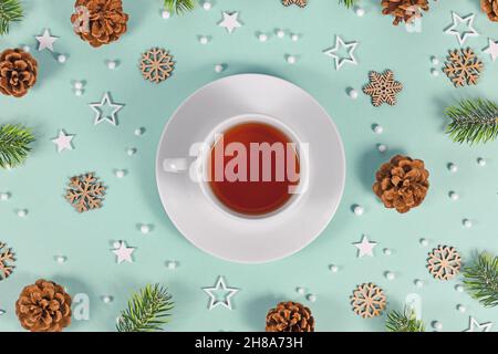 Tasse mit rotem Tee, umgeben von saisonaler Winterdekoration auf mintgrünem Hintergrund Stockfoto