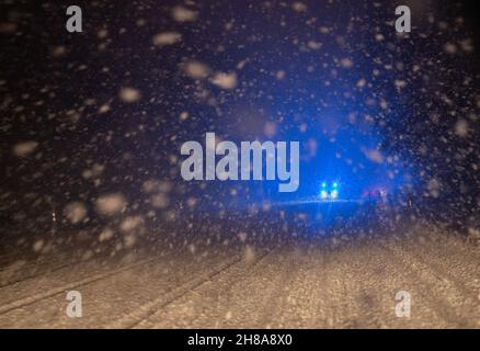 Stuttgart, Deutschland. 28th. November 2021. In einer starken Schneeverwehung fährt ein Auto mit blauem Licht auf einer schneebedeckten Straße. Quelle: Bernd Weißbrod/dpa/Alamy Live News Stockfoto