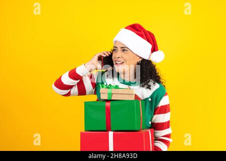 Porträt einer erwachsenen lateinerin, die mit dem Mobiltelefon in einem weihnachtskonzept auf gelbem Hintergrund telefoniert Stockfoto