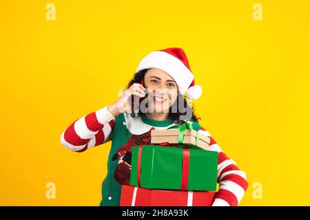 Porträt einer erwachsenen lateinerin, die mit dem Mobiltelefon in einem weihnachtskonzept auf gelbem Hintergrund telefoniert Stockfoto