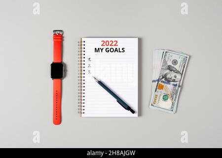 2022 Banner zu meinen finanziellen Zielen. Notizblock, Stift, Geldstapel und eine Tasse schwarzen Kaffee auf grauem Hintergrund isoliert. Notizblock mit Kopierbereich. Büro Stockfoto