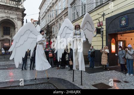 Prag, Tschechische Republik. 28th. November 2021. Künstler mit Engelsflügeln gehen auf der historischen Straße von Karlova.drei Künstler, die als Engel gekleidet sind, gehen auf Stelzen und bringen den Menschen am ersten Adventssonntag in Prag ihre fröhlichen Weihnachtswünsche. Kredit: SOPA Images Limited/Alamy Live Nachrichten Stockfoto