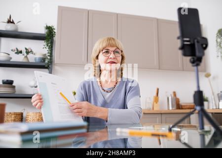 Erfahrene Wirtschaftslehrerin, die während des Livestreams für das Online-Publikum auf Finanzdokumente zeigt Stockfoto