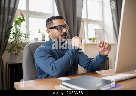 Zeitgemäßer Lehrer, der am Arbeitsplatz vor einem Computermonitor sitzt und während des Unterrichts sein Online-Publikum anschaut Stockfoto