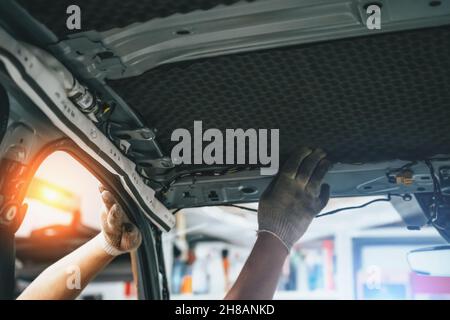 Arbeiter klebt Schalldämmmaterial auf die Innenseite des Autodachs. Prozess der Installation der Schalldämmung im Auto. Stockfoto