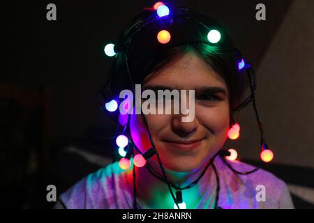 Lächelndes Porträt zu Weihnachten. Nahaufnahme verrückte glückliche junge Frau, die Weihnachten feiert. Junge Menschen haben Spaß in den Winterferien mit buntem Licht Stockfoto