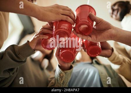 Blick aus der unteren Perspektive auf eine Gruppe von Teenagern, die mit Plastikbechern rösten und Cocktails auf einer Party trinken Stockfoto