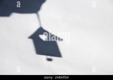 Unschärfe Schatten der Hand mit Weihnachtsspielzeug kleines Haus auf weißen Ziegelwand. Licht- und Schattenspielzeug. Haus Schatten mit Reflexion auf der weißen texturierten b Stockfoto