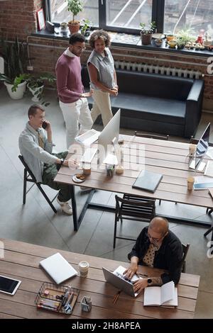 Zwei junge Kollegen, die an ihren Kollegen vorbeikommen, während sie im Büro unterwegs sind und Arbeitspunkte diskutieren Stockfoto