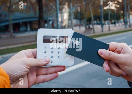 Weibliche Kundin ohne Gesicht, die NFC-Kauf mit Plastikkarte auf dem Terminal in der Stadtstraße macht Stockfoto