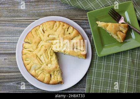Italienische Apfelkuchen auf einer Holztischplatte, in Scheiben geschnitten und auf einem quadratischen Teller auf einer grünen und währenden Serviette serviert Stockfoto