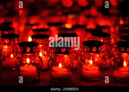 Viele Kerzen brennen in roten Kerzenhaltern in der Nacht Nahaufnahme Stockfoto