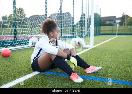 Großbritannien, müde weibliche Fußball-Torhüterin sitzt am Tor Stockfoto