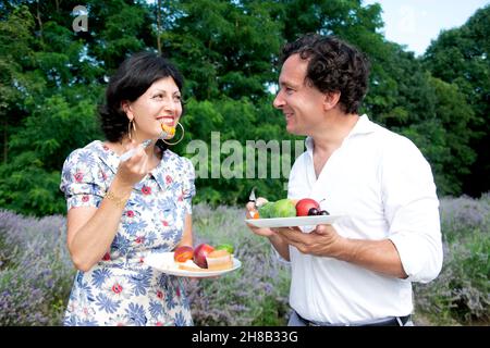 Lächelndes reifes Paar, das Früchte im Lavendelfeld isst Stockfoto