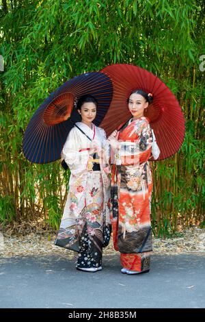 Porträt von zwei Frauen in Kimonos und mit Sonnenschirmen im Park Stockfoto