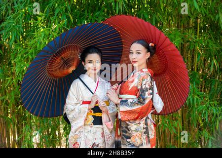 Porträt von zwei Frauen in Kimonos und mit Sonnenschirmen im Park Stockfoto