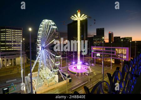 Nervenkitzel suchende Schreie, während sie sich auf dem beleuchteten Weihnachtsmarkt drehen und auf dem Riesenrad am Centenary Square, beleuchtet in der Dämmerung, nach Sonnenuntergang o Stockfoto
