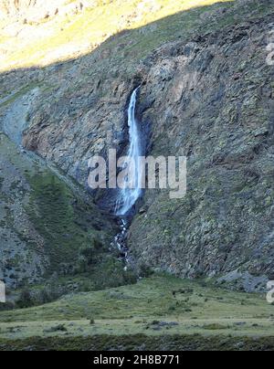 Ein kleiner Bach fließt in einem stürmischen Strom von einer hohen Klippe und spritzt sein Wasser auf die Hänge. Chulyshmanskaya-Tal, Altai, Sibirien, Russland. Stockfoto
