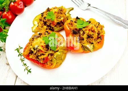 Pfeffer süß, gefüllt mit Pilzen, Tomaten, Couscous und Käse in einem weißen Teller auf Küchentuch, Gabel, Petersilie vor dem Hintergrund von Holz Stockfoto