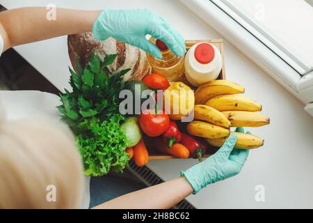 Frauenhände packen Lebensmittel in einen Karton, das Konzept der Unterstützung und Freiwilligenarbeit, Spende. Tragen Sie die medizinischen Schutzhandschuhe Stockfoto