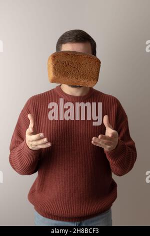 Ein Mann in einem Pullover wirft ein Stück Roggenbrot in die Luft. Vorderansicht. Hochformat. Stockfoto