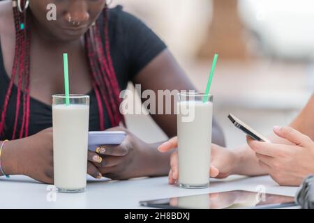 Nahaufnahme von zwei Gläsern Milchshakes auf dem Tisch, die von zwei Freunden im Freien getrunken werden Stockfoto
