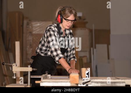 Junge Frau als Zimmermann mit Schutzbrille und Gehör Schutz funktioniert auf Hobelmaschine Stockfoto