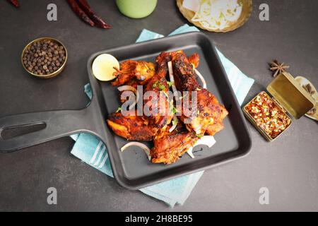 Tandoori-Huhn ist ein beliebtes Rezept für gebratenes Huhn aus Indien. Tandoor ist ein traditioneller Holzofen. Chicken Tandoori Platter wird auf einem schwarzen Teller serviert Stockfoto