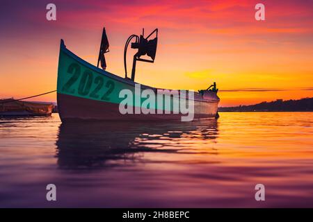 2022 Konzept. Fischerboot am Ufer und Wellenmeer bei dramatischem, farbenfrohen Sonnenuntergang Stockfoto