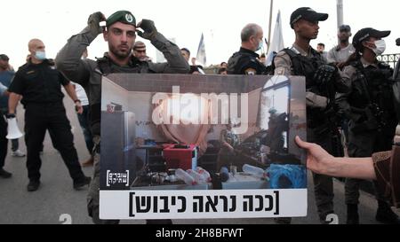 WESTJORDANLAND, Israel. 28th. November 2021. Ein Anhänger der linken Peace Now-Bewegung hält ein Schild mit einem Foto israelischer Soldaten in einem palästinensischen Haus, auf dem geschrieben steht: „so sieht die Besatzung aus“, während einer Demonstration gegen den Besuch des israelischen Präsidenten Isaac Herzog in der Ibrahimi-Moschee. Die Juden nennen sie die Höhle von Machpelah am Eingang der israelischen Siedlung Kiryat Arba in der Nähe der palästinensischen Stadt Hebron am 28. November 2021 im Westjordanland, Israel. Präsident Herzog besuchte den heiligen Ort, um die erste Chanukka-Kerze anzuzünden, ein Teil der Juden Stockfoto