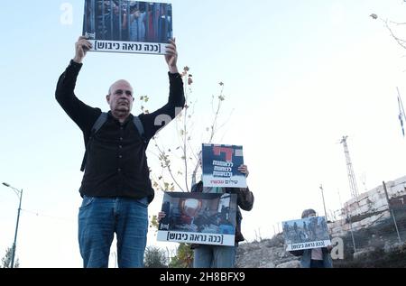 WESTJORDANLAND, Israel. 28th. November 2021. Anhänger der linken Peace Now-Bewegung halten während einer Demonstration gegen den Besuch des israelischen Präsidenten Isaac Herzog in der Ibrahimi-Moschee Schilder mit Fotos von israelischen Soldaten und Palästinensern mit der Aufschrift „so sieht die Besatzung aus“, Die Juden nennen sie die Höhle von Machpelah am Eingang der israelischen Siedlung Kiryat Arba in der Nähe der palästinensischen Stadt Hebron am 28. November 2021 im Westjordanland, Israel. Präsident Herzog besuchte die heilige Stätte, um die erste Chanukka-Kerze anzuzünden, die Teil des jüdischen Feiertags war. Stockfoto