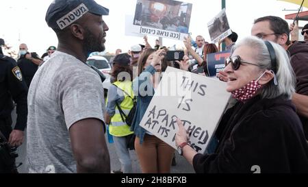 Ein israelischer linker Aktivist hält während einer Demonstration gegen den Besuch des israelischen Präsidenten Isaac Herzog in der Ibrahimi-Moschee ein Schild vor einem Polizisten mit der Aufschrift: „Dies ist die Apartheid in ihrer schlimmsten Form“. Die Juden nennen sie die Höhle von Machpelah am Eingang der israelischen Siedlung Kiryat Arba in der Nähe der palästinensischen Stadt Hebron am 28. November 2021 im Westjordanland, Israel. Präsident Herzog besuchte die heilige Stätte, um die erste Chanukka-Kerze anzuzünden, die Teil des jüdischen Feiertags war. Palästinenser und linke Israelis äußerten ihre Missbilligung Stockfoto