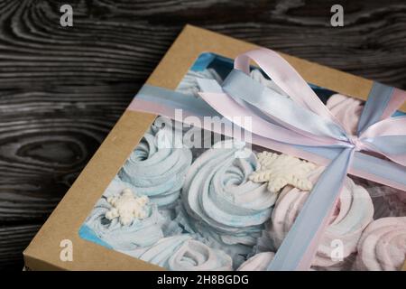 Marshallow blau und rosa. Liegt in handwerklichen Verpackungen. Dekoriert mit mastistischen Schneeflocken. Die Box ist mit einem Band gebunden, das an einen Bogen gebunden ist. Auf schwarzem Kiefernbrett Stockfoto