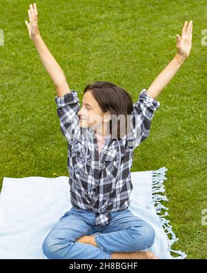 Portrait junge schöne Brünette Mädchen hat Spaß in einem Sommerpark. Ein süßes Schulmädchen sitzt auf dem Gras auf einer Tagesdecke und genießt einen warmen Sommertag Stockfoto