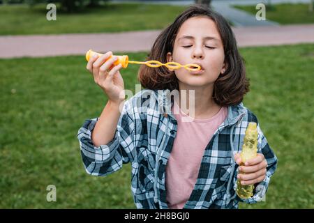 Nette Schülerin der kaukasischen Ethnie bläst Seifenblasen. Porträt eines attraktiven schönen Brünette Mädchen Spaß in einem Sommerpark. Positiv em Stockfoto