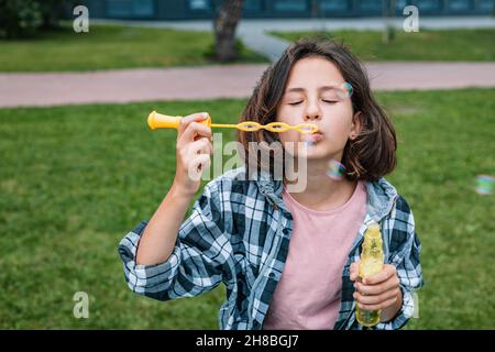 Attraktive Schülerin der kaukasischen Ethnie macht Seifenblasen. Porträt eines niedlichen schönen Brünette Mädchen Spaß in einem Sommerpark. Positive Emot Stockfoto