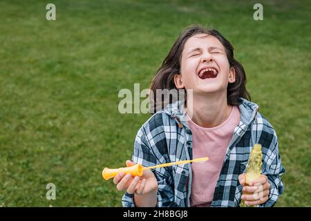 Porträt eines niedlichen schönen Brünette Mädchen Spaß in einem Sommerpark. Lachende Schülerin kaukasische Ethnie mit Seifenblasen. Frohe Kindheit. Po Stockfoto