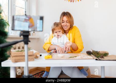 Portrait der jungen Mutter und ihrer kleinen Tochter machen Spielzeug für die Weihnachtsferien. Defokussed Smartphone im Vordergrund. Das Konzept von vi Stockfoto