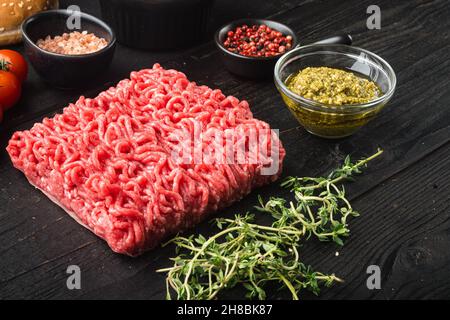 Rohes Hackfleisch mit Gewürzen, Gemüse und Kräutern und Fleischbällchen, auf schwarzem Holztischhintergrund Stockfoto