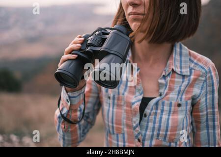 Porträt einer unerkennbaren jungen Frau, die mit einem Fernglas in den Händen unterwegs ist. Stockfoto