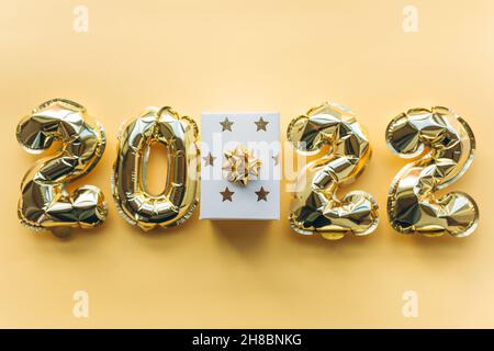 Luftballons aus Goldfolie in Form von Zahlen 2022 und Geschenkbox auf einem goldenen Hintergrund. Stockfoto