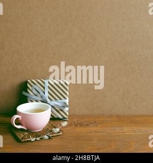 Geschenkbox und Tasse Tee auf Holztisch. Braune Wandhintergrund. Jubiläumskonzept Stockfoto