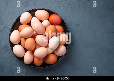 Frische Hühnereier auf einem Teller auf dunklem Grund. Draufsicht, Kopierbereich. Stockfoto